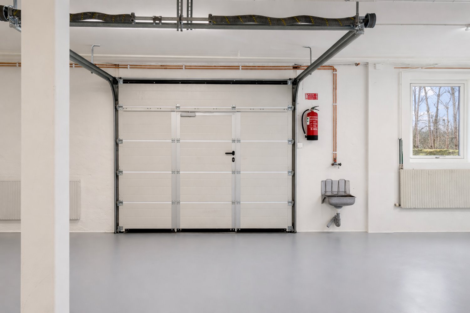 Lagerdel med port som möjliggör smidig in- och utlastning. Nymålade väggar och golv skapar en ljus och välskött arbetsmiljö.