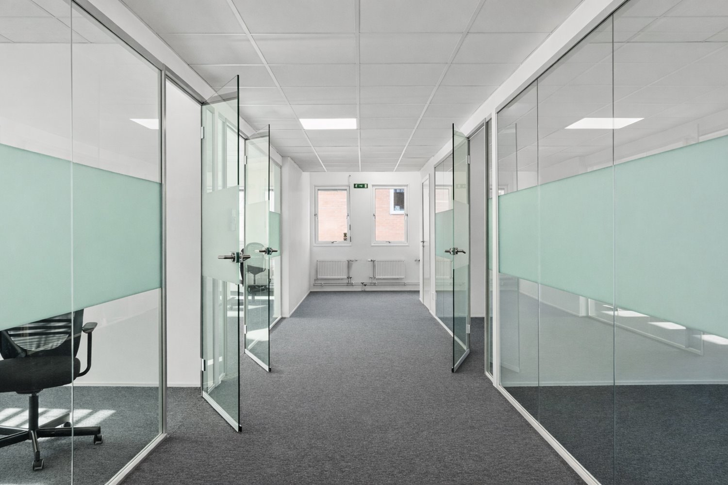 Modern korridor med stilrena glasade kontorsrum som skapar ett öppet och professionellt intryck. Glaspartierna släpper in ljus och ger en luftig kontorsmiljö.