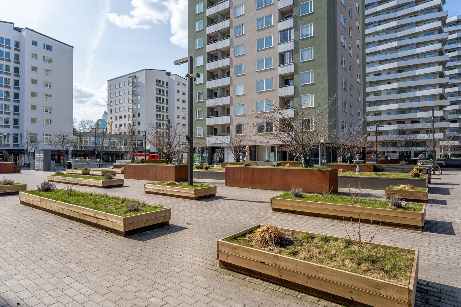 Öppen och modern platsbildning omgiven av bostäder och verksamheter som ger ett starkt lokalt upptagningsområde.