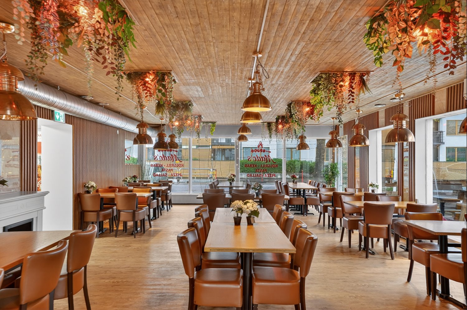 Restaurang med generösa sällskapsytor, varm atmosfär och stora fönster som skapar en inbjudande miljö för gästerna.